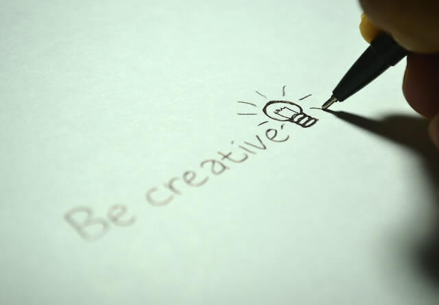 L'immagine di una persona che scrive la parola "creatività" con una penna o una matita, simboleggia l'atto di esprimere e promuovere la creatività attraverso la comunicazione scritta.